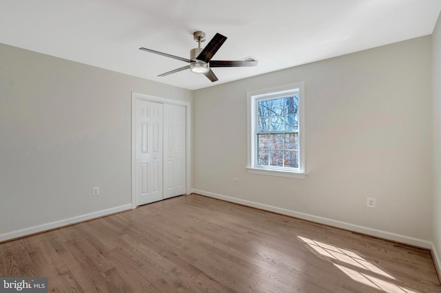 unfurnished bedroom featuring a closet, wood finished floors, a ceiling fan, and baseboards