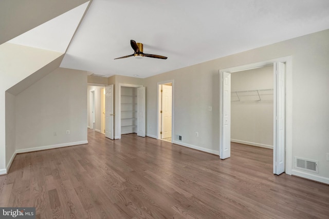 unfurnished bedroom with a walk in closet, wood finished floors, visible vents, and baseboards