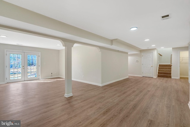 below grade area featuring light wood-style floors, french doors, baseboards, and stairs