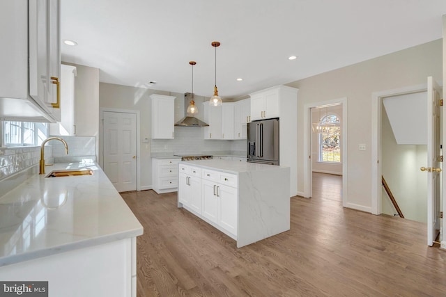 kitchen with plenty of natural light, appliances with stainless steel finishes, light wood-type flooring, wall chimney range hood, and a sink