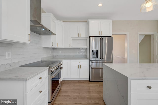 kitchen with light stone counters, stainless steel appliances, backsplash, wall chimney range hood, and light wood-type flooring