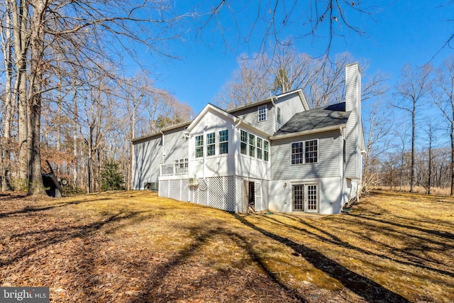 rear view of house with a yard, a chimney, a sunroom, and french doors