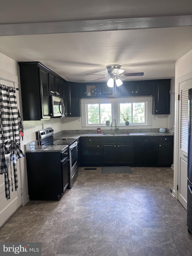 kitchen with appliances with stainless steel finishes, a sink, ceiling fan, dark stone countertops, and dark cabinets