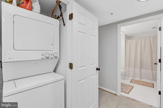 clothes washing area featuring light tile patterned floors, laundry area, and stacked washer / drying machine