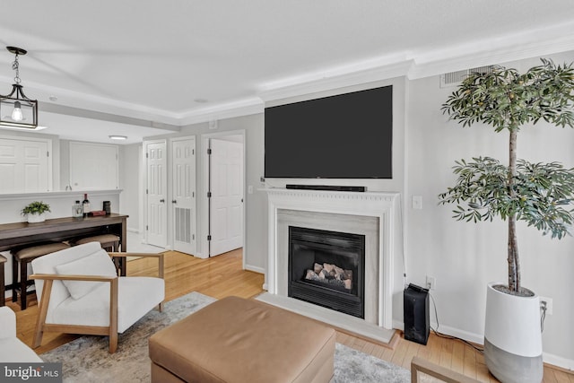 living area featuring crown molding, a fireplace, light wood-style flooring, and baseboards