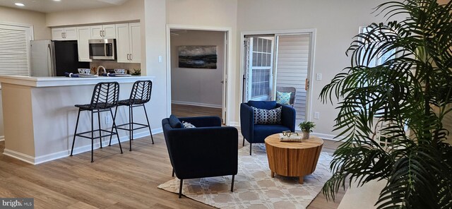 interior space featuring baseboards, a breakfast bar, appliances with stainless steel finishes, light wood-style floors, and white cabinetry