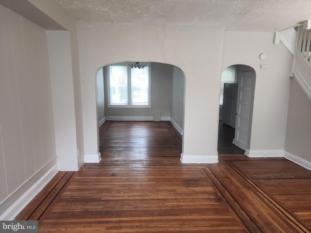 unfurnished room with arched walkways, a textured ceiling, wood finished floors, and baseboards