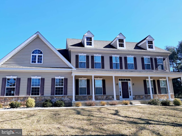 view of front of house with stone siding, covered porch, and a front yard