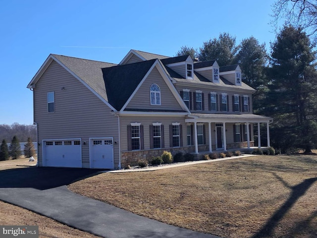 view of front facade featuring aphalt driveway, a porch, an attached garage, a front yard, and stone siding