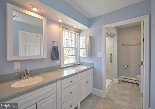 bathroom featuring a sink, baseboard heating, double vanity, and toilet