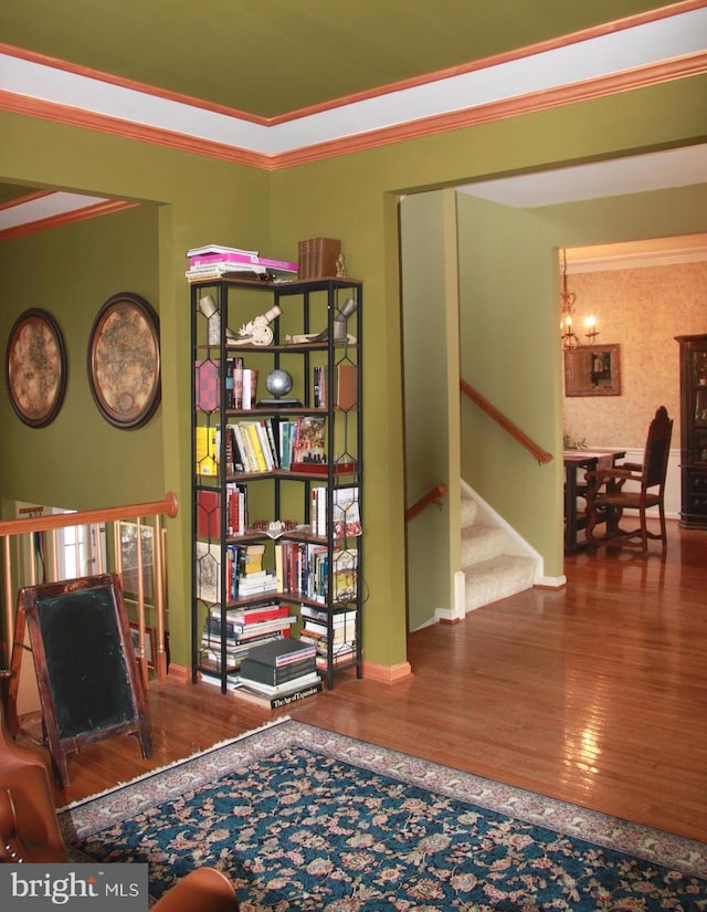 sitting room featuring a notable chandelier, ornamental molding, wood finished floors, stairway, and baseboards