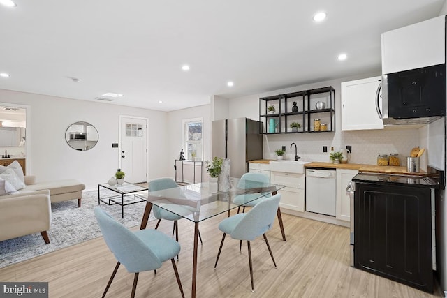 kitchen with white dishwasher, a sink, light wood-style flooring, and white cabinets