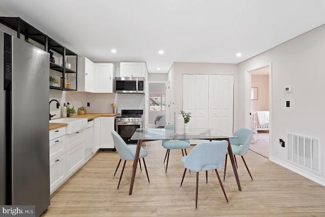 kitchen featuring open shelves, stainless steel appliances, visible vents, backsplash, and a sink