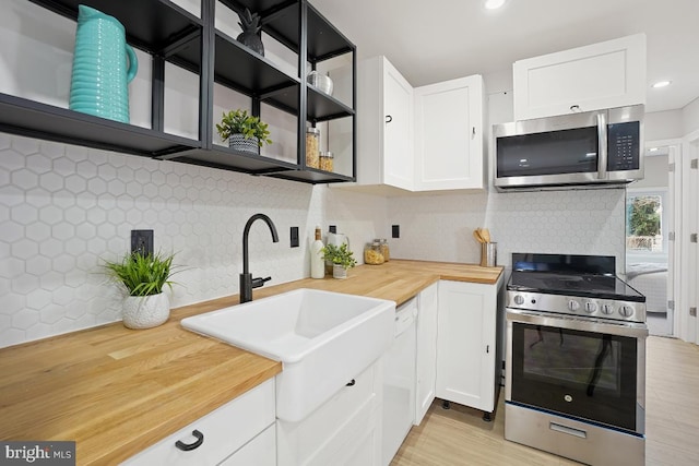 kitchen with backsplash, appliances with stainless steel finishes, white cabinetry, a sink, and butcher block countertops