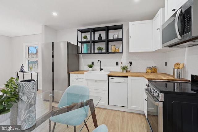 kitchen with wood counters, appliances with stainless steel finishes, white cabinets, and a sink