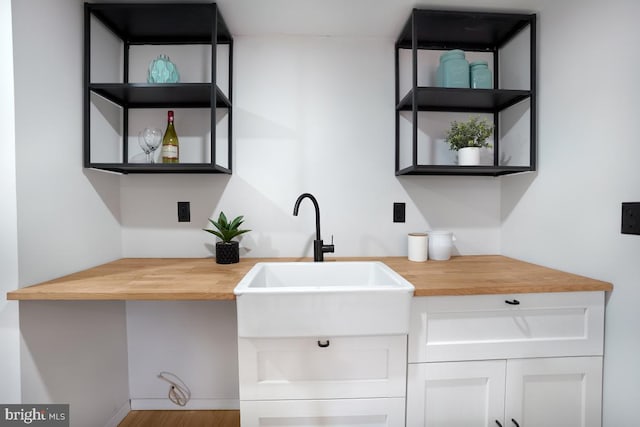 kitchen with white cabinets, wooden counters, a sink, and open shelves