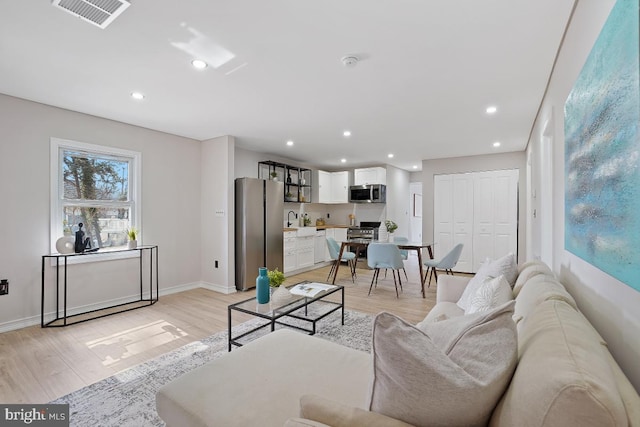 living area with recessed lighting, visible vents, light wood-style flooring, and baseboards