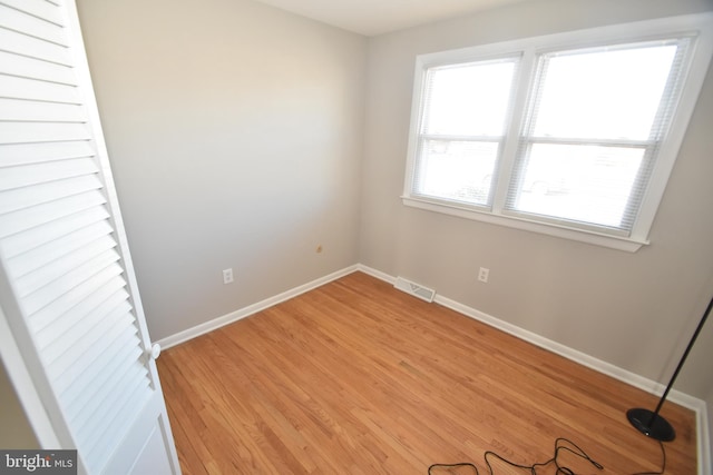 empty room with light wood-style floors, visible vents, and baseboards