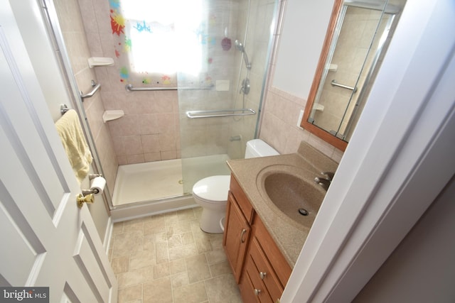 bathroom with tile walls, toilet, a stall shower, stone finish floor, and vanity