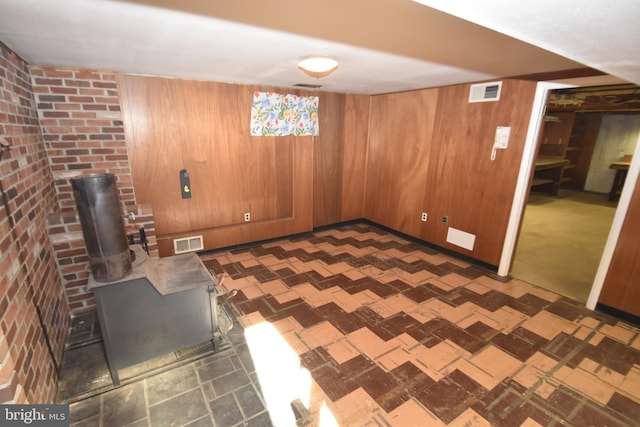 finished basement featuring a wood stove, wood walls, and visible vents