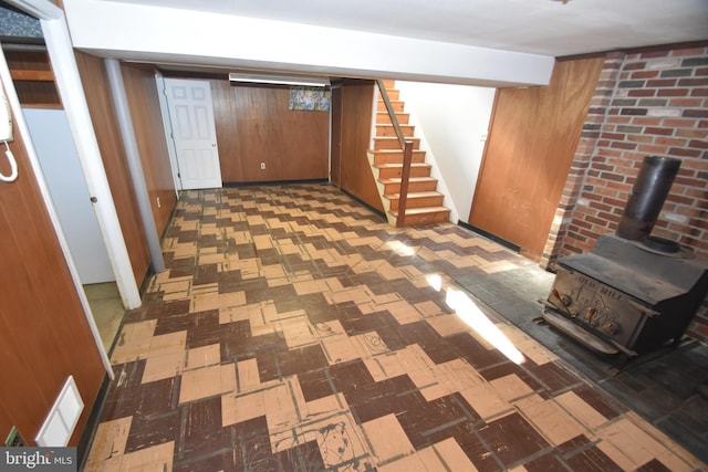 finished basement featuring wood walls, visible vents, stairway, tile patterned floors, and a wood stove