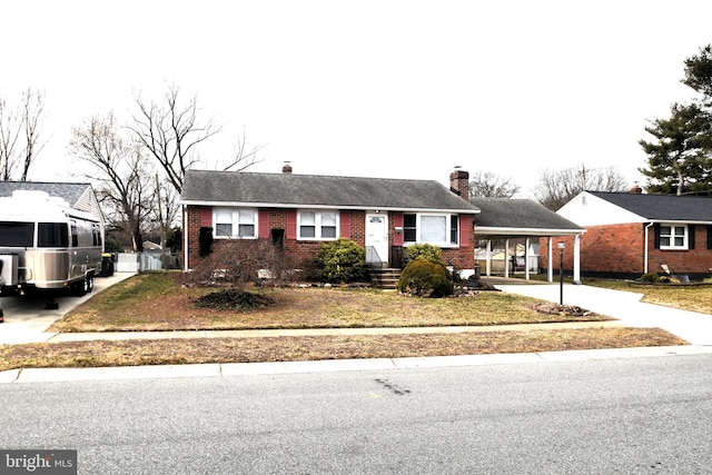 ranch-style house featuring a carport, concrete driveway, brick siding, and a chimney