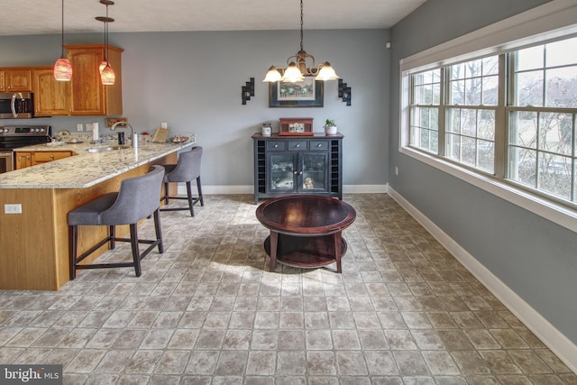 kitchen with baseboards, brown cabinets, stainless steel appliances, a kitchen bar, and a sink