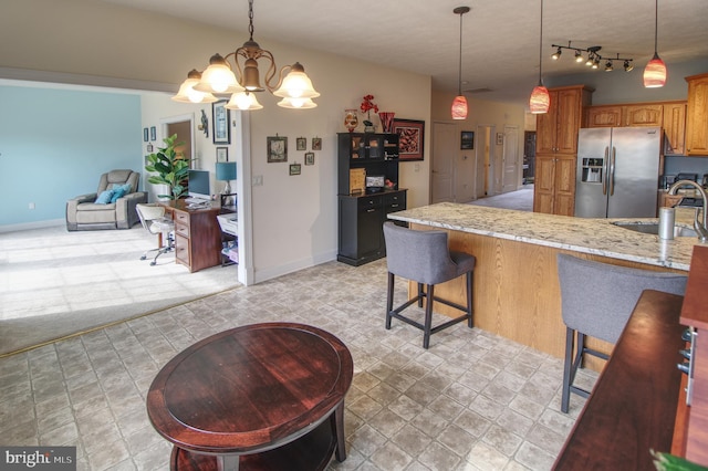 kitchen with a sink, hanging light fixtures, stainless steel fridge with ice dispenser, brown cabinetry, and a kitchen bar