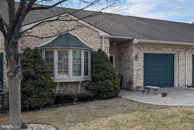 view of front facade featuring a shingled roof, an attached garage, and brick siding