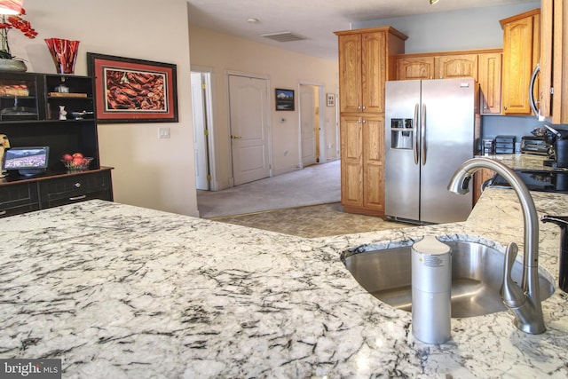 kitchen with light stone counters, visible vents, a sink, and stainless steel fridge with ice dispenser