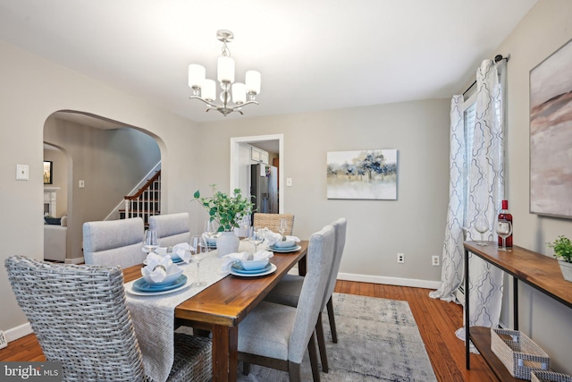 dining area with arched walkways, wood finished floors, baseboards, stairs, and an inviting chandelier