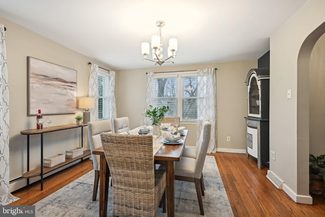 dining room with arched walkways, a chandelier, wood finished floors, visible vents, and baseboards