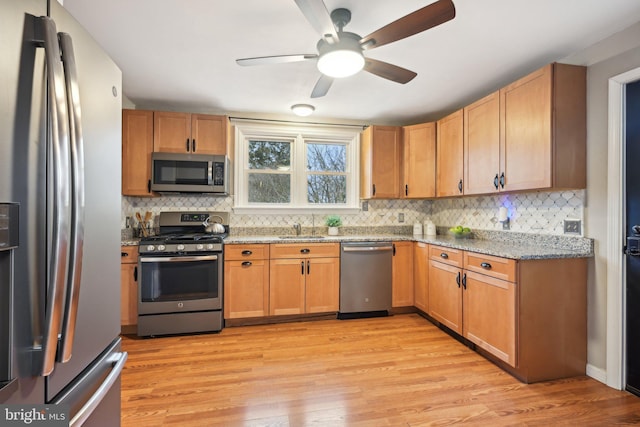 kitchen with light wood finished floors, appliances with stainless steel finishes, decorative backsplash, and light stone counters