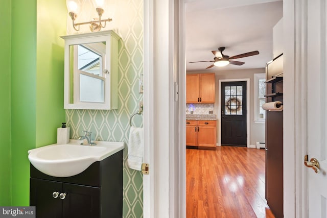 bathroom featuring ceiling fan, a baseboard radiator, wood finished floors, vanity, and wallpapered walls