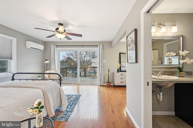 bedroom with a wall unit AC, a sink, wood finished floors, access to outside, and baseboards