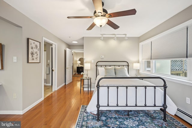 bedroom featuring a baseboard heating unit, light wood-type flooring, track lighting, and baseboards