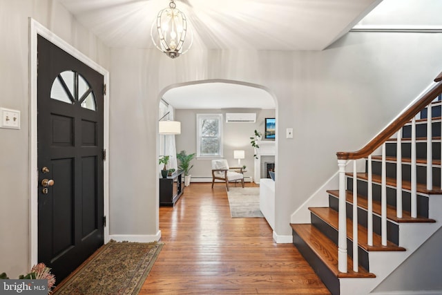 foyer with stairs, a warm lit fireplace, an AC wall unit, and wood finished floors