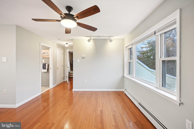 unfurnished room featuring a baseboard radiator, rail lighting, light wood-style flooring, and baseboards