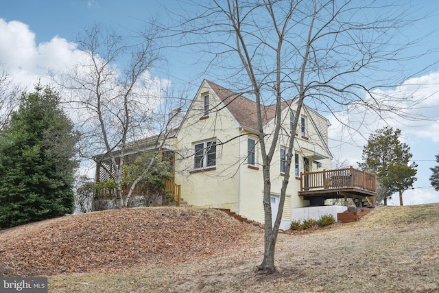 view of home's exterior with a shingled roof, a wooden deck, and stucco siding