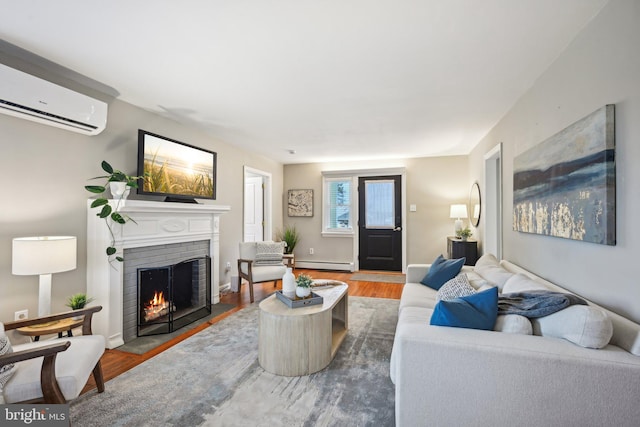 living room with a baseboard heating unit, wood finished floors, baseboards, an AC wall unit, and a brick fireplace