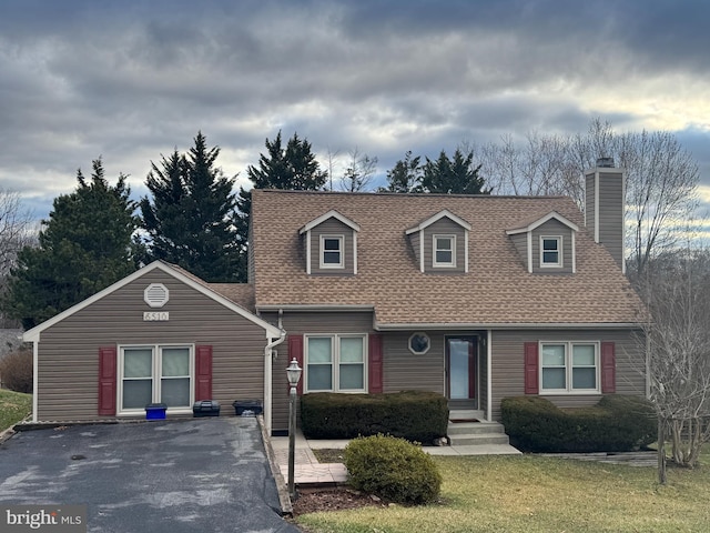 new england style home featuring a front lawn, a chimney, and roof with shingles