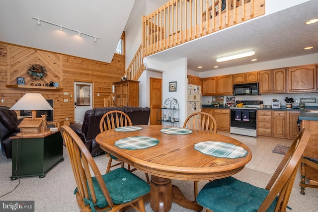 dining space featuring recessed lighting, a high ceiling, wood walls, stairway, and track lighting