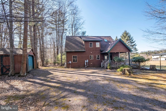 back of house featuring a garage, covered porch, roof with shingles, and an outbuilding