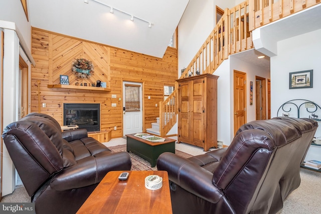 living area with wooden walls, a glass covered fireplace, stairs, a high ceiling, and carpet floors