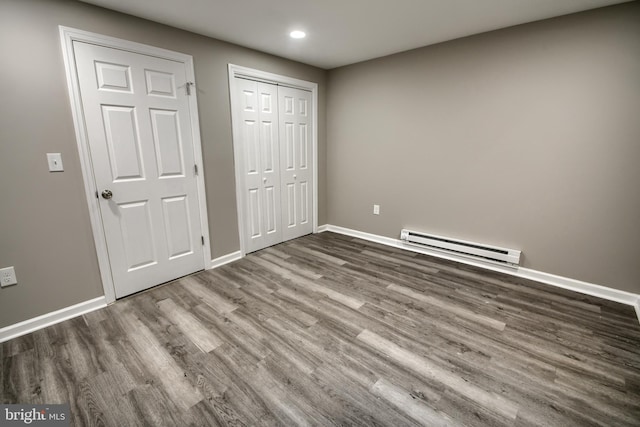 unfurnished bedroom with a baseboard heating unit, a closet, baseboards, and wood finished floors