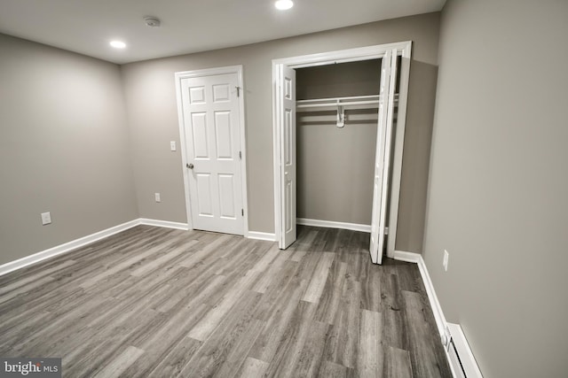 unfurnished bedroom with a baseboard radiator, a closet, recessed lighting, wood finished floors, and baseboards