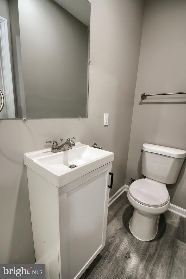 half bathroom featuring baseboards, vanity, toilet, and wood finished floors