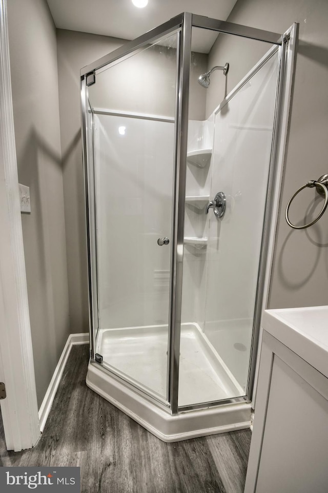 full bath featuring a shower stall, baseboards, and wood finished floors