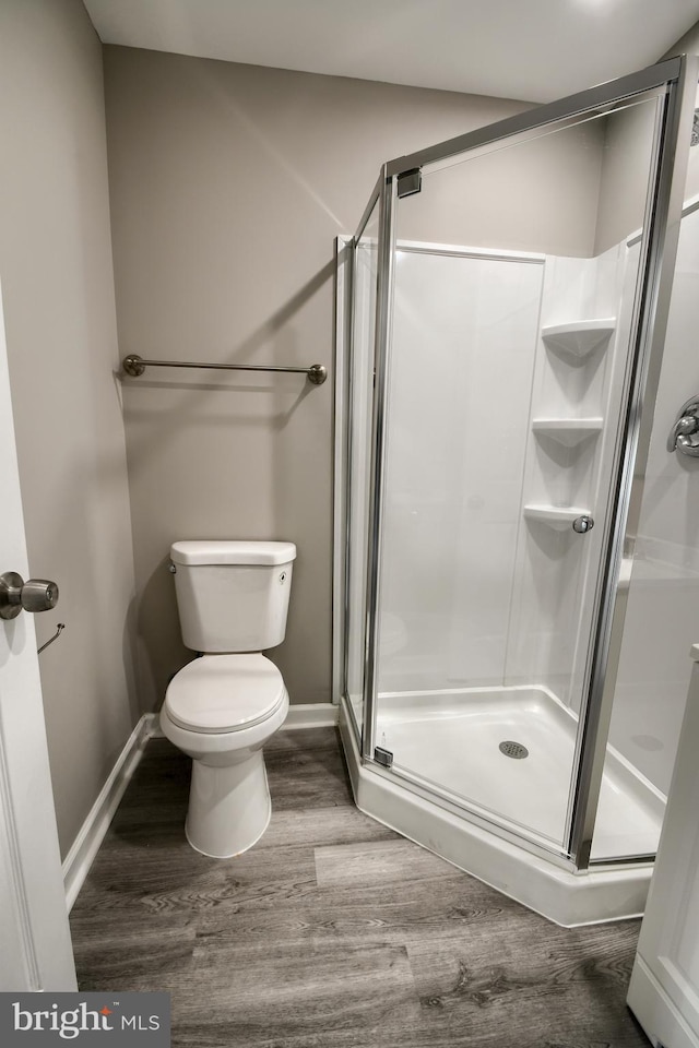 full bath with a stall shower, wood finished floors, toilet, and baseboards