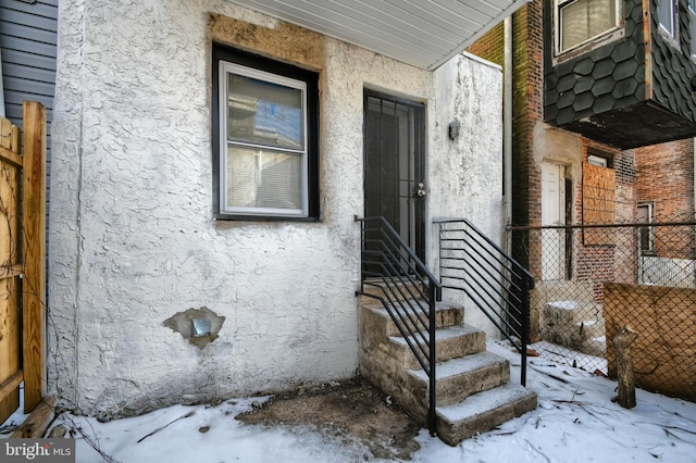 snow covered property entrance with stucco siding